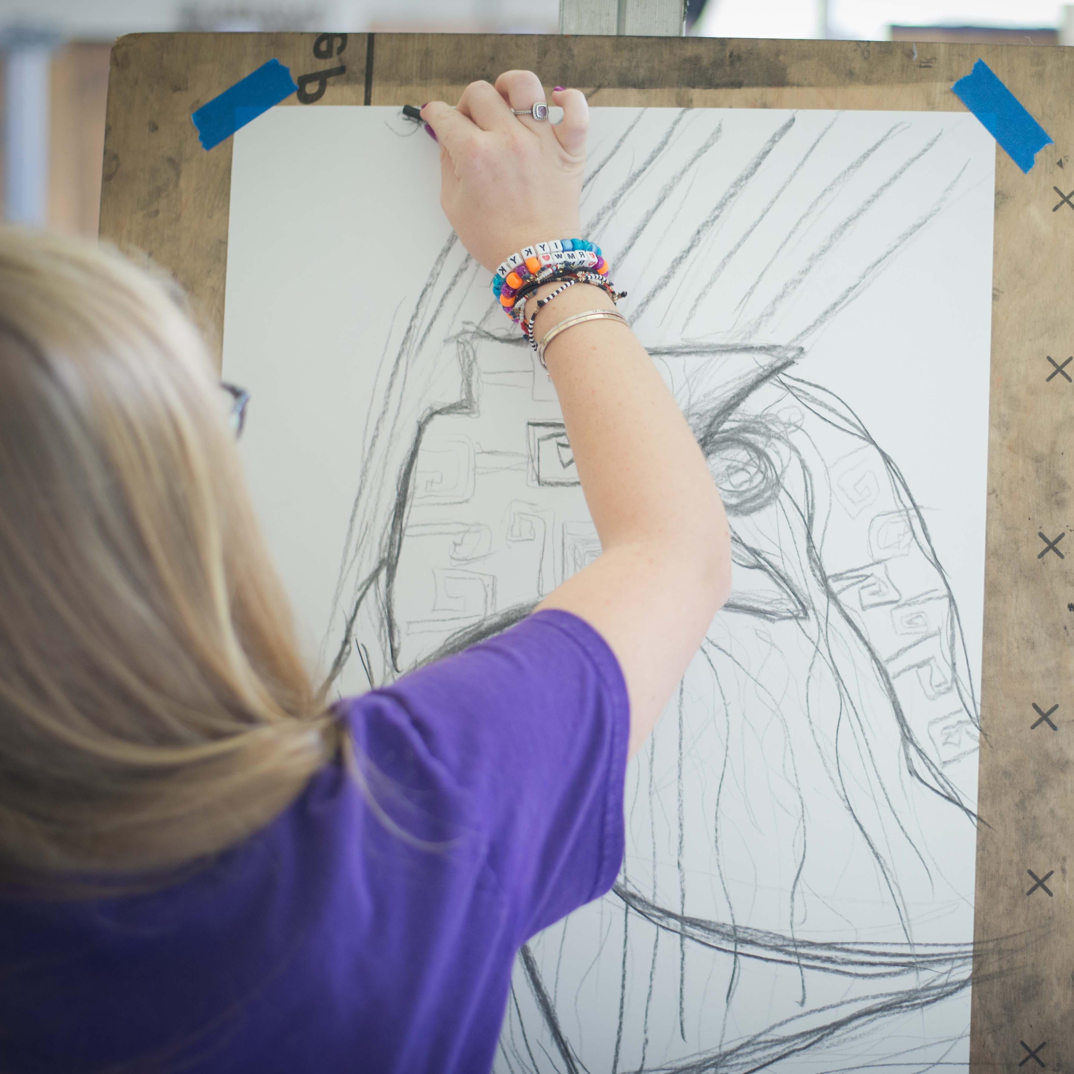 A student sk等hes on paper taped to an easel